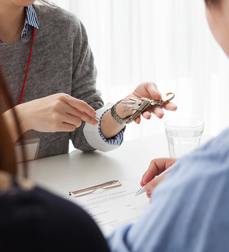 A woman hands keys to a man during a discussion over a rental agreement, with a glass of water on the table A woman hands keys to a man during a discussion over a rental agreement, with a glass of water on the table