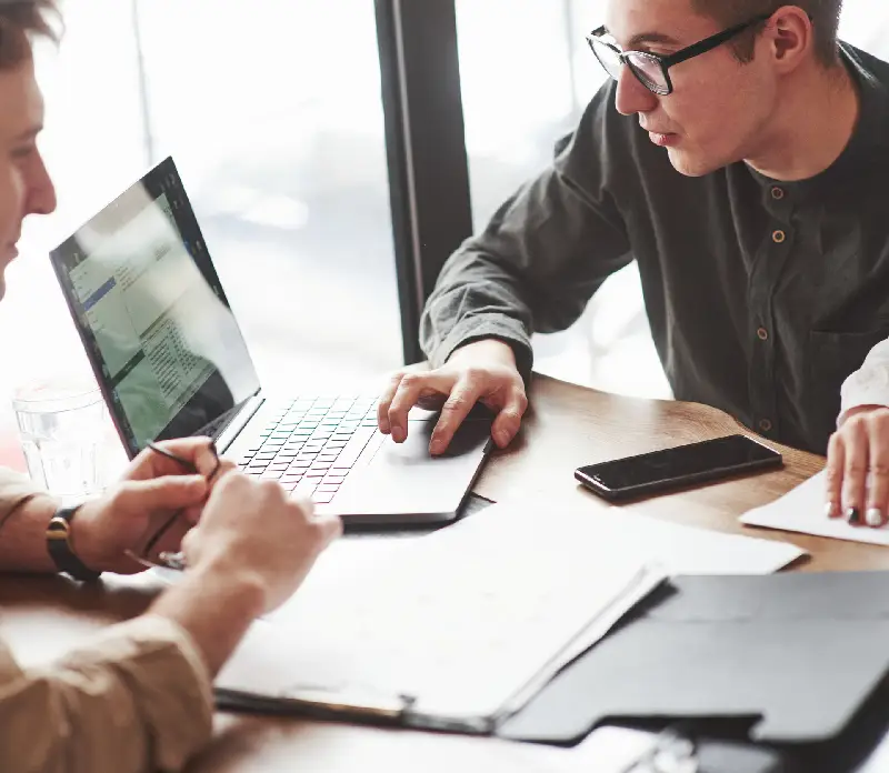 A group of people collaborates over a laptop and papers at a wooden table A group of people collaborates over a laptop and papers at a wooden table