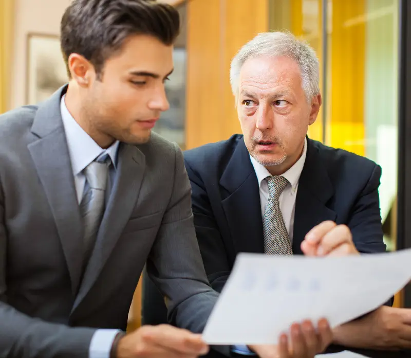 Two professionals in suits engage in a discussion, amidst a bright office environment with warm lighting Two professionals in suits engage in a discussion, amidst a bright office environment with warm lighting